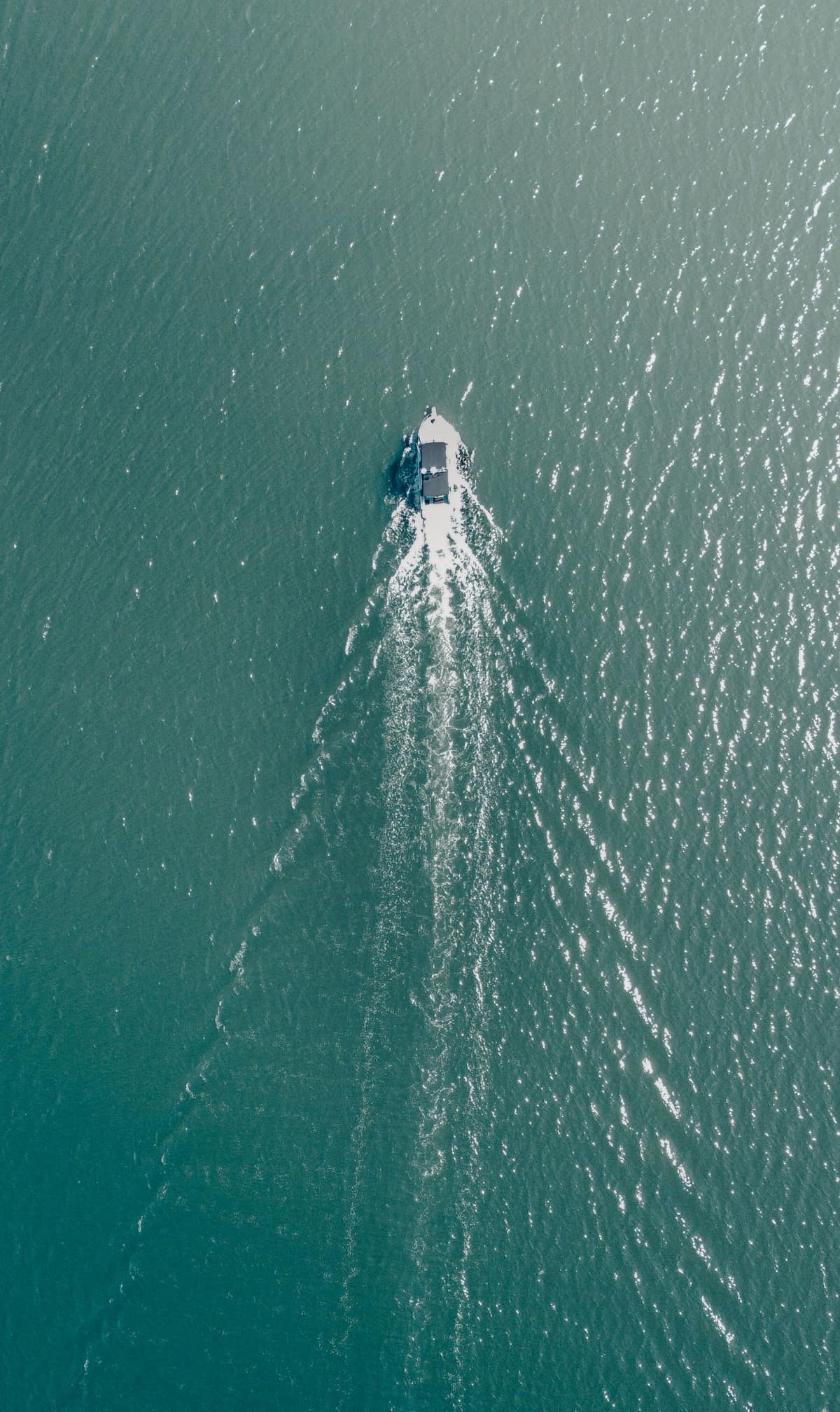 Photo: a boat under way seen from above, wake spreading across open water